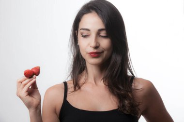 Koyu saçlı güzel beyaz kız gri arka planda iki çilekle oynuyor.