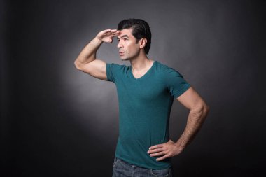 Koyu renk saçlı, yeşil tişörtlü adam koyu arka planda izole edilmiş.