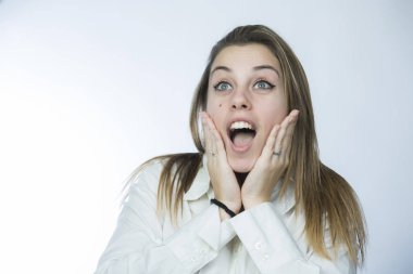 Beyaz tişörtlü sarışın kız ellerini yüzüne koyar ve şaşkınlıkla yüzünü çevirir.