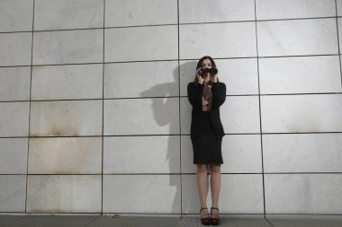 Siyah takım elbiseli esmer kadın yönetici, elindeki dürbünle diğer tarafa bakıyor, beyaz dikdörtgen duvar arka planında izole edilmiş.