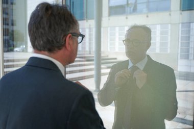 Takım elbiseli ve kravatlı yönetici modern şehir ortamını düzenleyen cam pencereye yansıdı