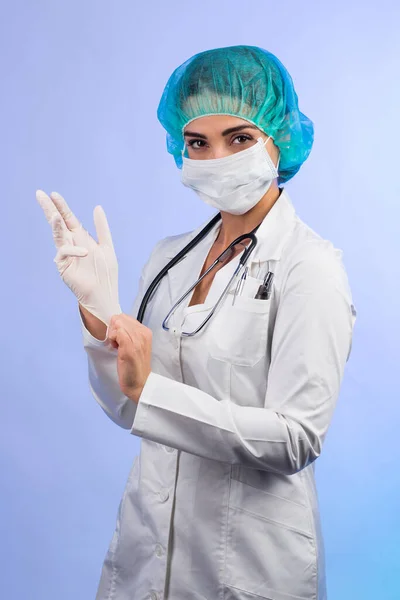 身穿白衣 戴白色面罩 头戴绿色帽子的女医生决心戴上乳胶手套 与白色背景隔离 — 图库照片