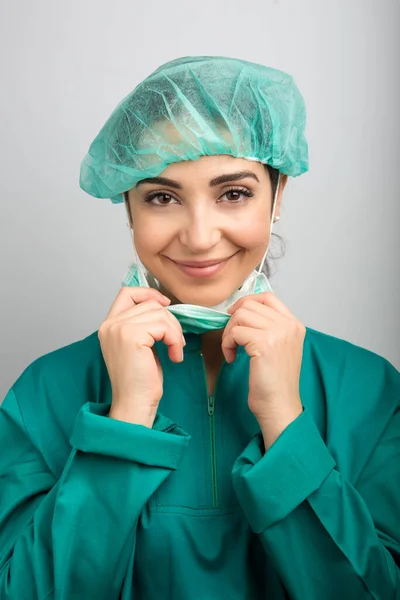 緑のキャップ 緑のコート マスクを持つ歯科医は カメラの笑顔を見て 灰色の背景 — ストック写真
