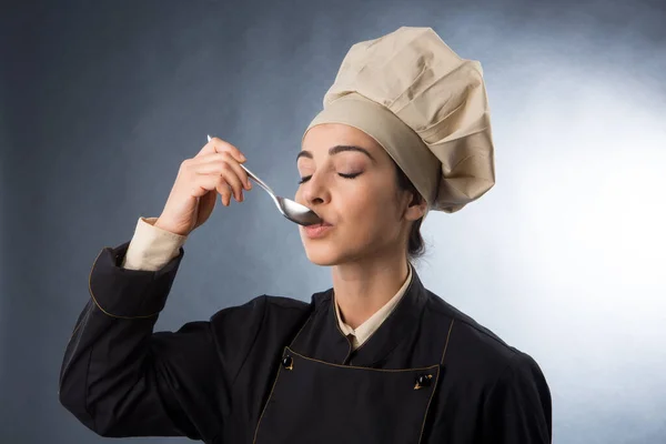 女厨师从勺子里尝一道菜 用灰色背景隔开 — 图库照片