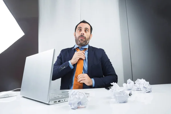 ノートパソコンの前の職場に座ってるエレガントなスーツのマネージャーがオレンジ色のカルバッタを面白い顔で手配してる — ストック写真