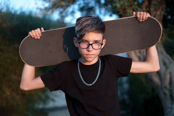 Nastolatek Okularach Wygląda Poważnie Trzymając Deskorolkę Głową — Zdjęcie stockowe
