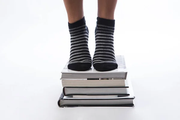 脚上有条纹的脚趾袜和堆叠书籍的女足的细部 白色背景 — 图库照片