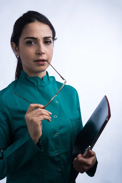 身穿绿色外套的女医生拿着一个黑色文件夹和眼镜 严肃地望着 与白色背景隔离 — 图库照片