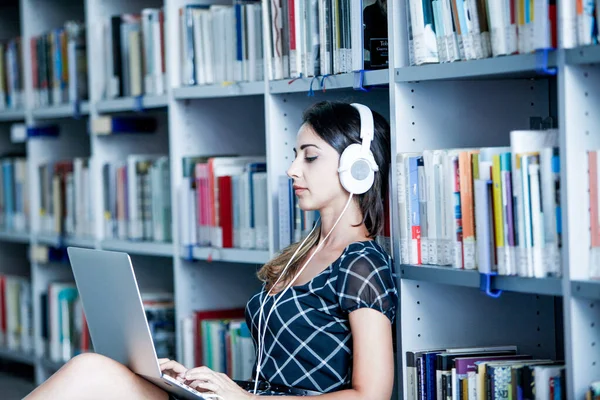 图书馆里带着耳机和笔记本电脑的年轻女子 — 图库照片