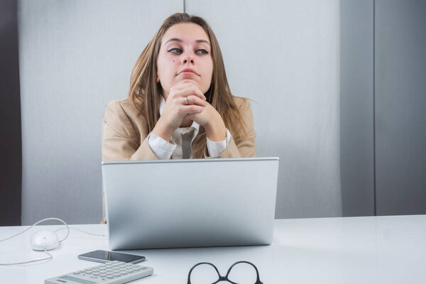 blonde girl dressed in a beige jacket is sitting at her workstation in front of the portal she absents herself dreamily