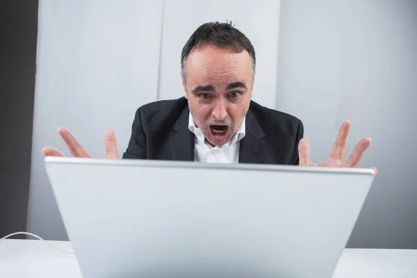 五十岁的经理穿着衬衫和黑色夹克坐在他的工作站上 对他的笔记本电脑很生气 — 图库照片