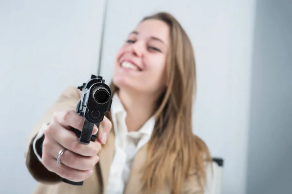 ブロンドの女の子はベージュのジャケットを着て彼女のワークステーションに座っています彼女はそれを使用する準備ができて彼女の手に銃を持っています — ストック写真