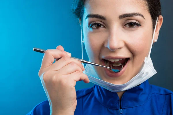 Dentystka Masce Chirurgicznej Niebieskim Płaszczu Pokazuje Narzędzia Pracy Odizolowane Jasnoniebieskim — Zdjęcie stockowe