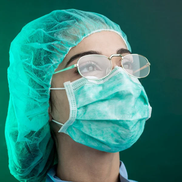 身穿蓝色实验室服 头戴绿色手术室帽 戴着面部外科口罩的医生从他的眼镜中看起来很严肃 与绿色背景隔离 — 图库照片