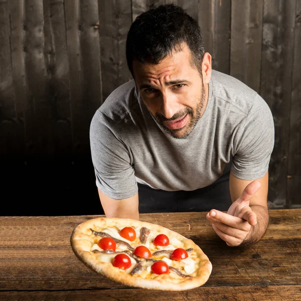一个留着胡子的黑头发男人正要吃一个带有樱桃西红柿的披萨 它是木制背景的 — 图库照片