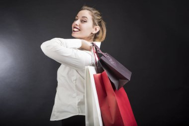 Uzun sarı saçlı, beyaz gömlekli güzel bir kız alışveriş için siyah arka planda duruyor.