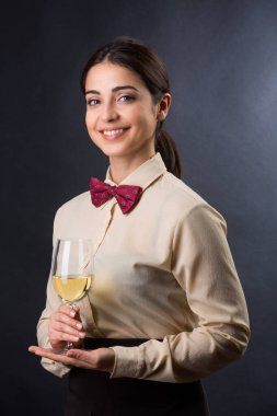Gömleği ve kırmızı papyonu olan güzel ve zarif garson siyah arka planda izole edilmiş bir müşteriye bir bardak şarap sunmaya hazır.
