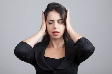 Siyah giysili beyaz kız, ellerini umutsuzluk içinde, gri arka planda soyutlanmış bir şekilde kafasına getiriyor.