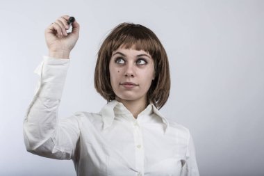 Kısa saçlı bir kız, görünmez bir duvarda işaretli bir şey çiziyor, beyaz bir arka planda izole edilmiş.