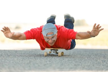 Kırmızı formalı son sınıf öğrencisi bir kır yolunda kaykay yapmaktan hoşlanıyor.