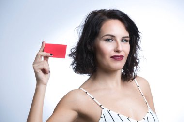 Beyaz çizgili tulumlu, siyah saçlı beyaz kadın beyaz arka planda izole edilmiş kırmızı bir kartı işaret ediyor.