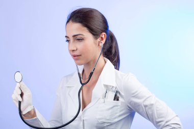 Beyaz önlüklü kadın doktor steteskopu hafif bir arka planda test ediyor.
