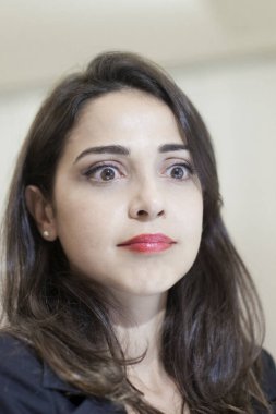 İş yerinde gergin bir ifadeyle oturan esmer bir müdürün portresi.