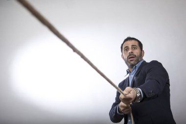 Koyu renk saçlı yönetici, beyaz arka planda izole edilmiş, rekabetin değerlerini ve başarının çabasını sembolize etmek için zorla bir halat çekiyor.