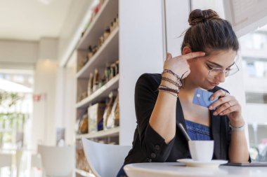 Masada oturan koyu renk saçlı bir kız tabletini tutuyor ve kredi kartıyla internetten bir şeyler almaya hazır. İfade belirsizliklerden biridir..