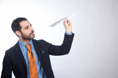 Koyu saçlı, sakallı, gömlekli, turuncu ceketli ve kravatlı bir adam, beyaz arka planda izole edilmiş, kağıt bir uçağı havaya fırlatıyor.