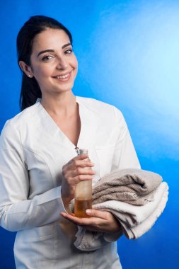 Saçları toplanmış esmer kız mavi arka planda izole edilmiş havlular getiriyor.