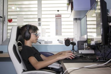 Evinde elektronik oyunlar oynayan kulaklıklı ve klavyeli genç bir çocuk.