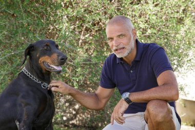 Mavi polo tişörtlü kel adam evdeki bahçede köpeğiyle oynuyor.