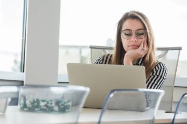 Çizgili gömlekli ve gözlüklü sarışın sekreter çalışma yerinde ofisinde oturuyor.