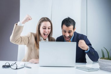 Bir çift iş arkadaşı, masanın önünde dizüstü bilgisayarla oturarak elde edilen sonuçlardan memnun. Siyah bir arkaplanda izole edilmiş.