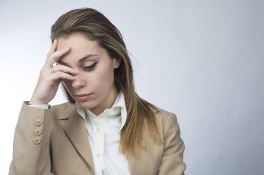 Bej ceketli sarışın kadın menajer el ele verip, depresif bir ifadeyle, beyaz arka planda izole bir şekilde aşağıya bakıyor.