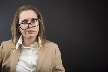 Yüzünde çarpık gözlüklerle, siyah arka planda izole edilmiş bej renkli zarif ceketli bir portre kadın.