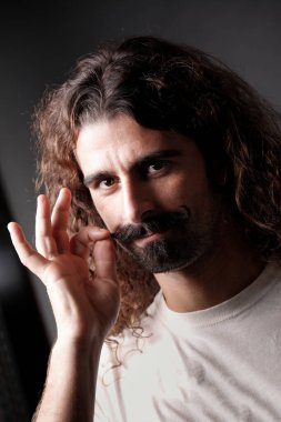 Gidonlu bıyıklı ve uzun saçlı bir adam ciddi görünüyor, karanlık arka planda soyutlanmış.