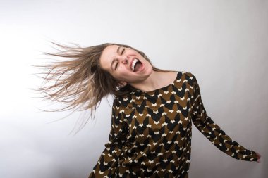 Tişörtlü komik kız dans ediyor ve beyaz arka planda saçlarını çılgın gibi oynatarak müzik aleti çalıyormuş gibi yapıyor.