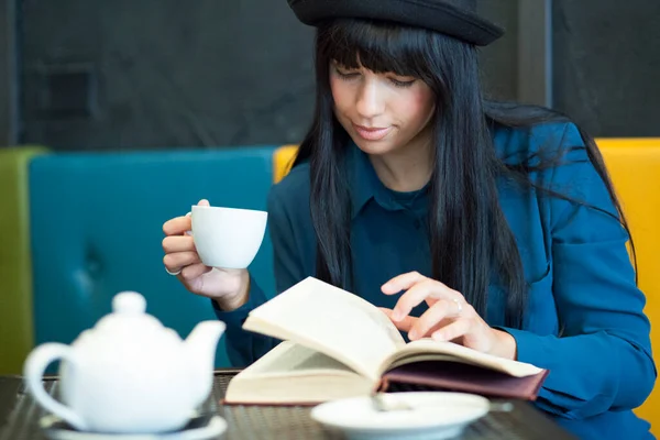 穿着白衬衫和黑色牛仔裤的小女孩坐在咖啡店里看书 — 图库照片
