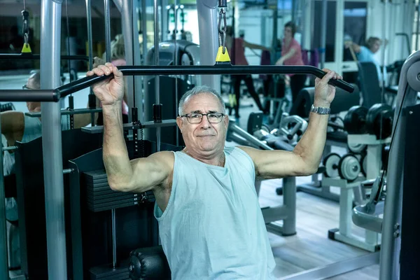 上了年纪的人在健身房里用机器训练 并在后面做运动 — 图库照片