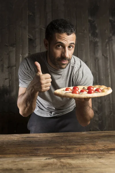 髭を生やした黒髪の男は 木の背景に隔離されたチェリートマトとピザを食べることになっています — ストック写真