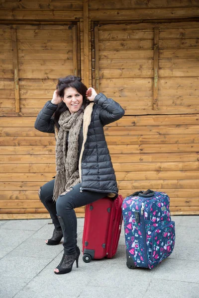 穿着冬衣的游客正坐在一个正方形的木制小亭前的行李箱上 — 图库照片
