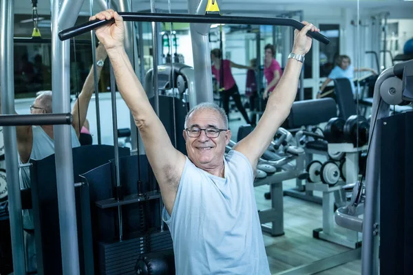 上了年纪的人在健身房里用机器训练 并在后面做运动 — 图库照片