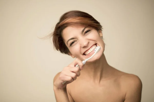 beautiful girl with short hair brushes her teeth with a toothbrush, isolated on light background