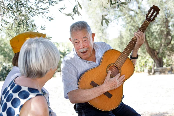 senior couple playing guitar in park