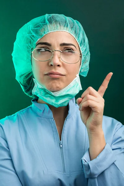 身穿蓝色实验室外套 戴着白色面罩的医生绝望地把手伸向他的头 双手被绿色背景隔开 — 图库照片
