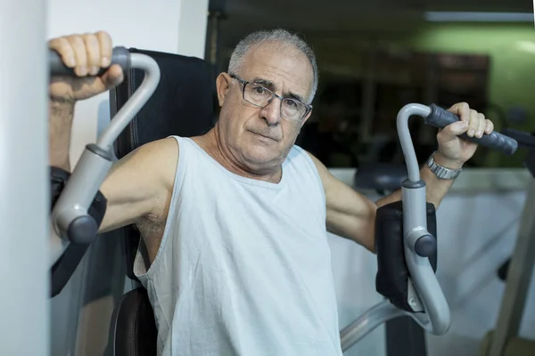 上了年纪的男人 带着浅蓝色的油箱 在健身房的机器上进行着顶级的训练 — 图库照片