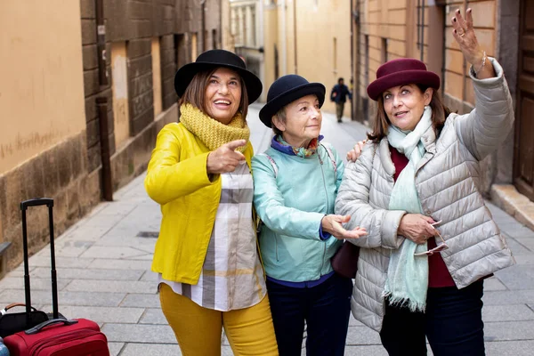 带着帽子和彩色衣服的老年游客们带着手提箱在城市里游玩 — 图库照片
