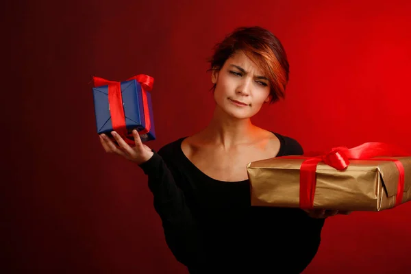 黒のシャツを着た美しい少女レッドの背景に隔離された2つのプレゼントが手に包まれるのを喜んでいる — ストック写真